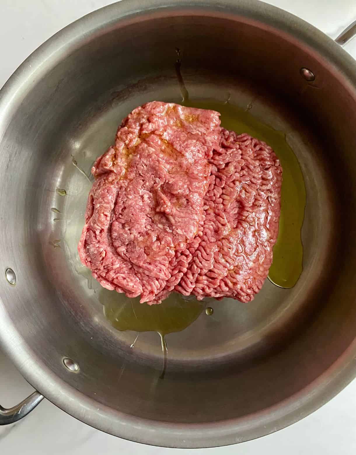 A pot with olive oil and raw ground beef.