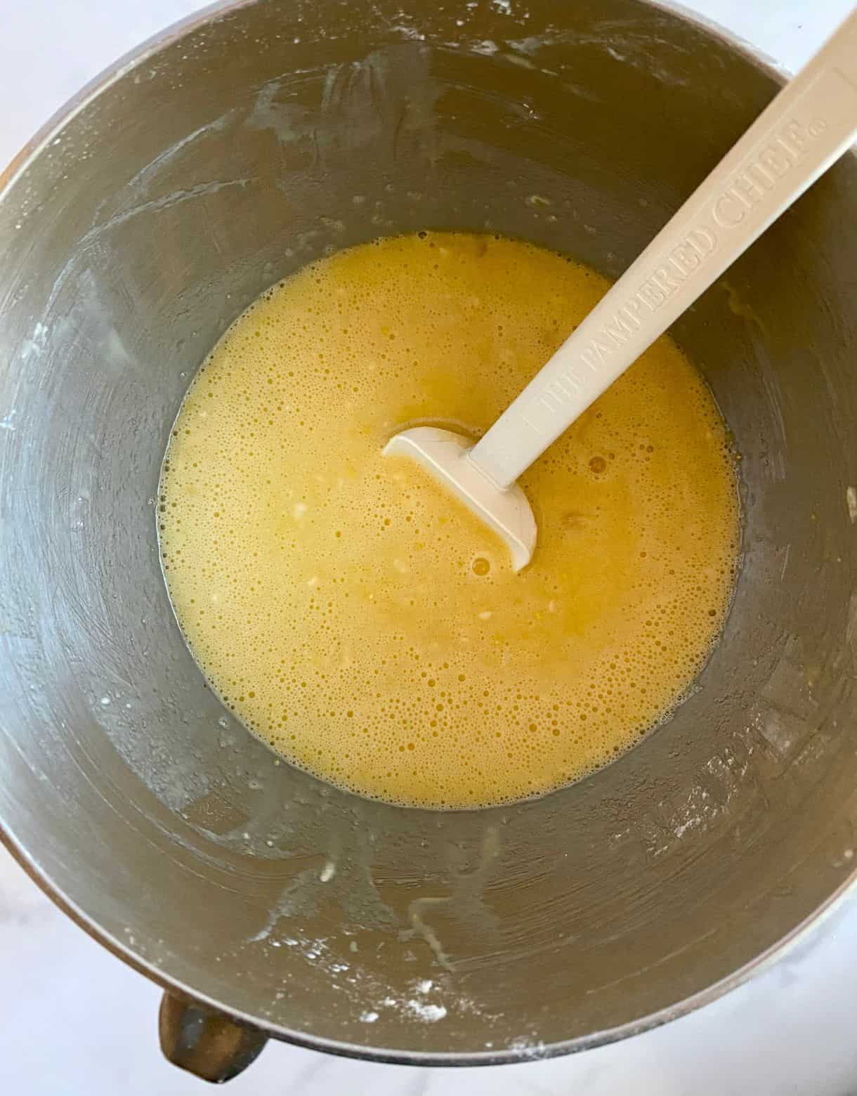 A mixing bowl with eggs, sugar, flour, lemon juice and lemon zest stirred together.