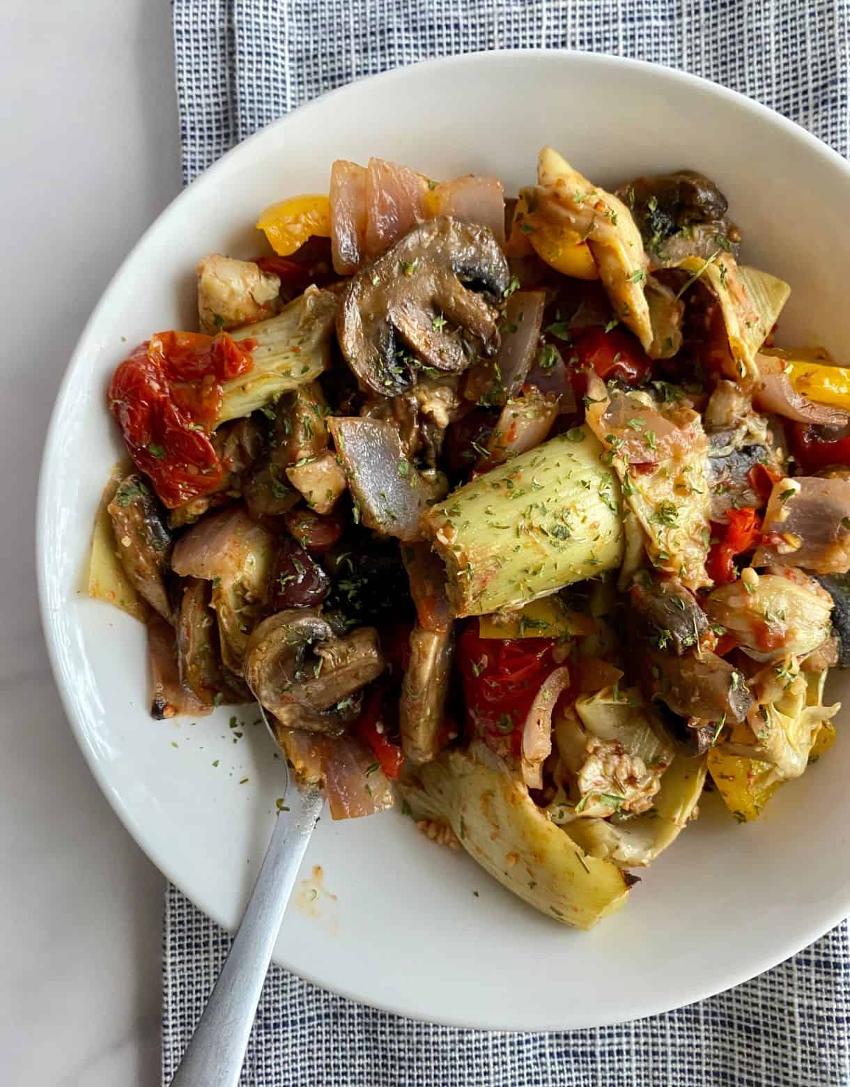 A bowl of cooked Mediterranean Roasted Vegetables with mushrooms, onions, bell peppers, tomatoes and artichoke hearts.