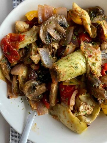 A plate of cooked Mediterranean Roasted Vegetables with mushrooms, tomatoes, onion, bell pepper and artichokes.