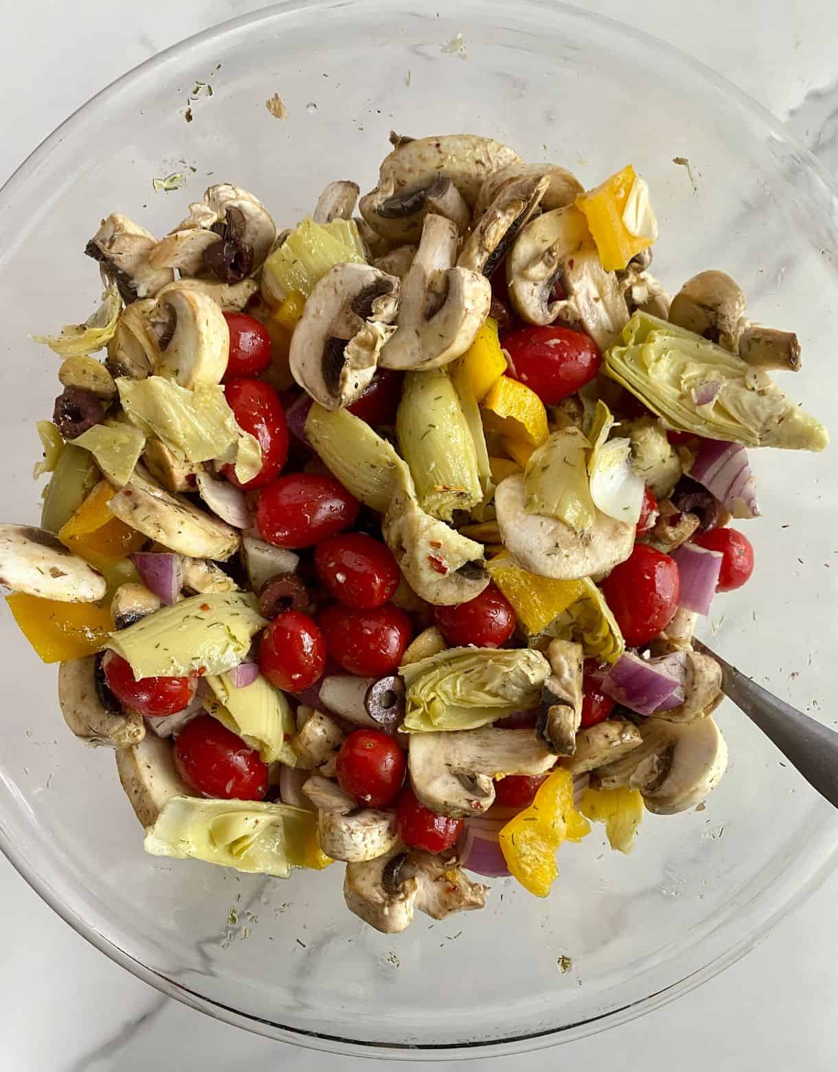 A bowl of assorted raw vegetables tossed with oil and spices.