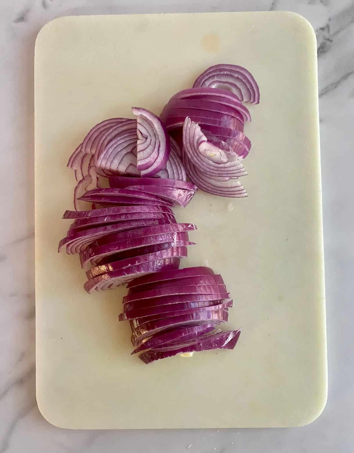A cutting board with 2 red onions, thinly sliced.