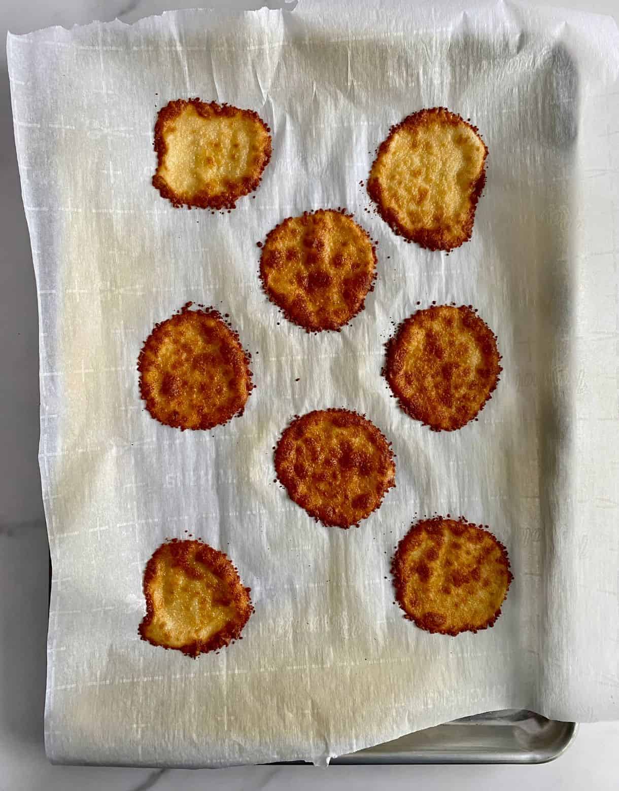 A sheet pan lined with parchment with cooked parmesan crisps.