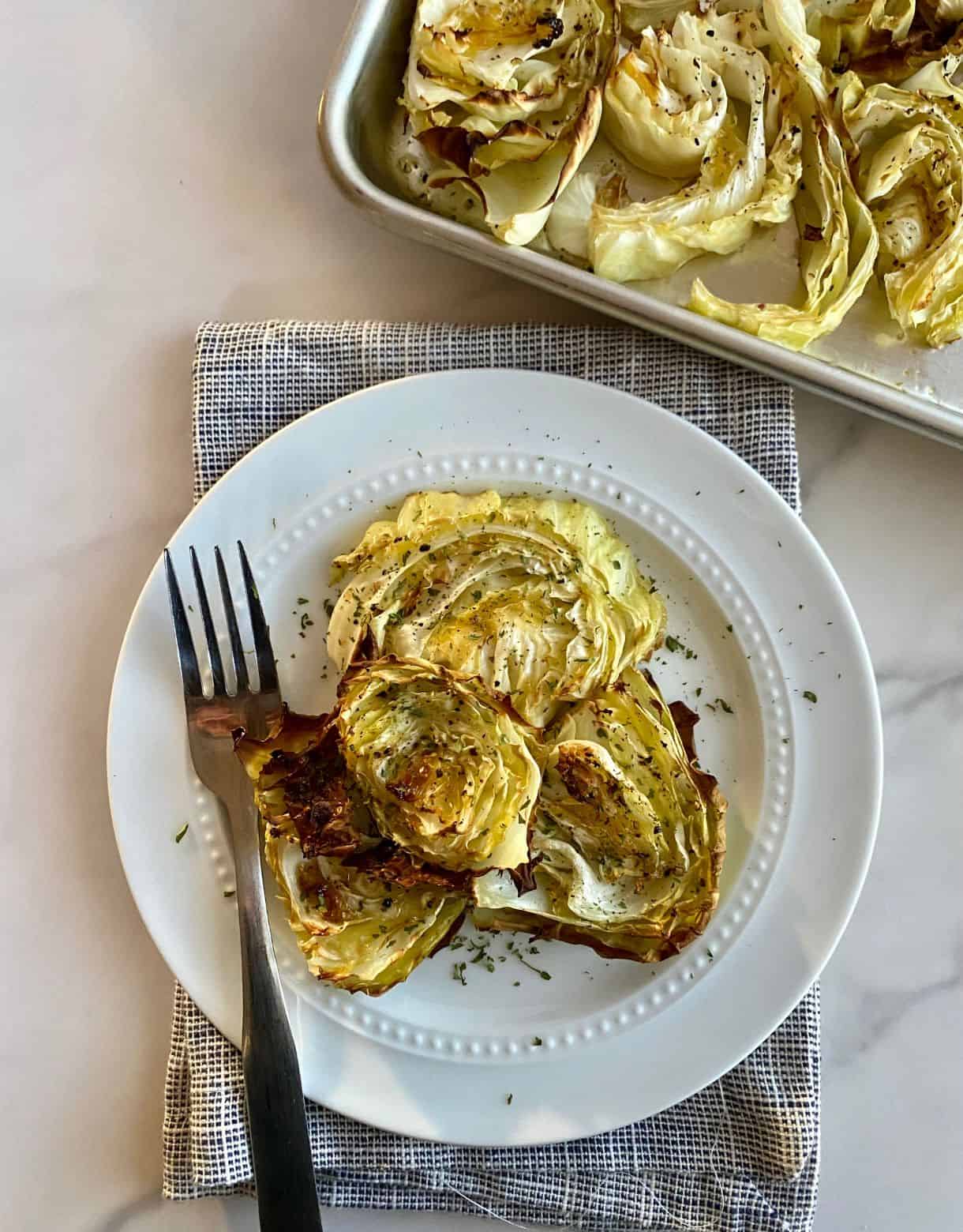 A plate with cooked Oven Roasted Cabbage Steaks and a fork.