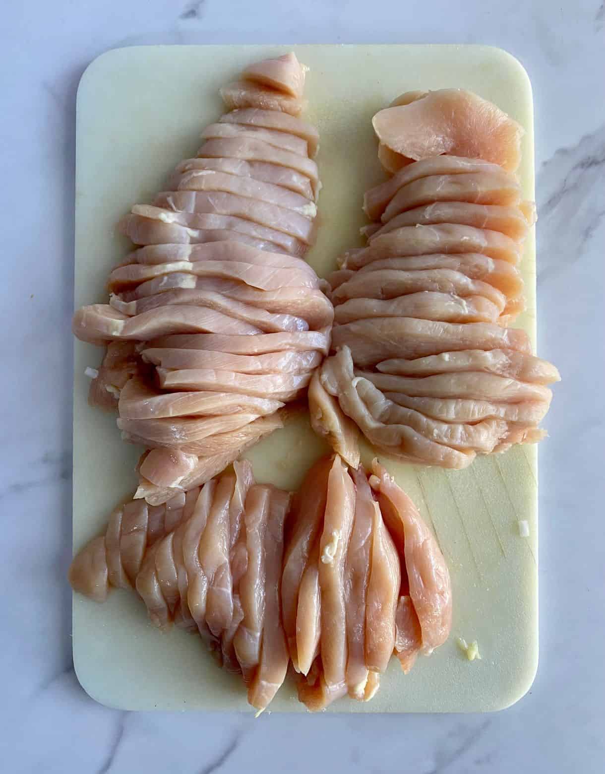 A cutting board with sliced raw chicken.