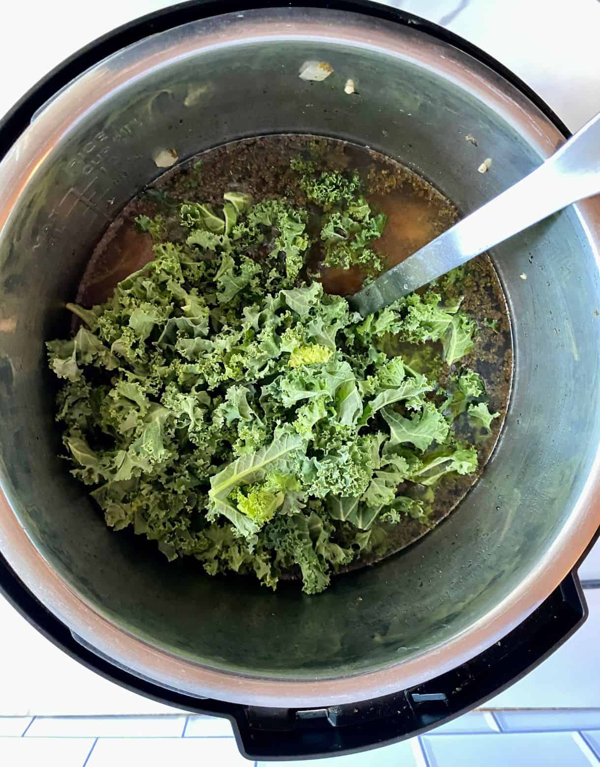 A slow cooker of Chicken Kale Soup with the kale added but not stirred.