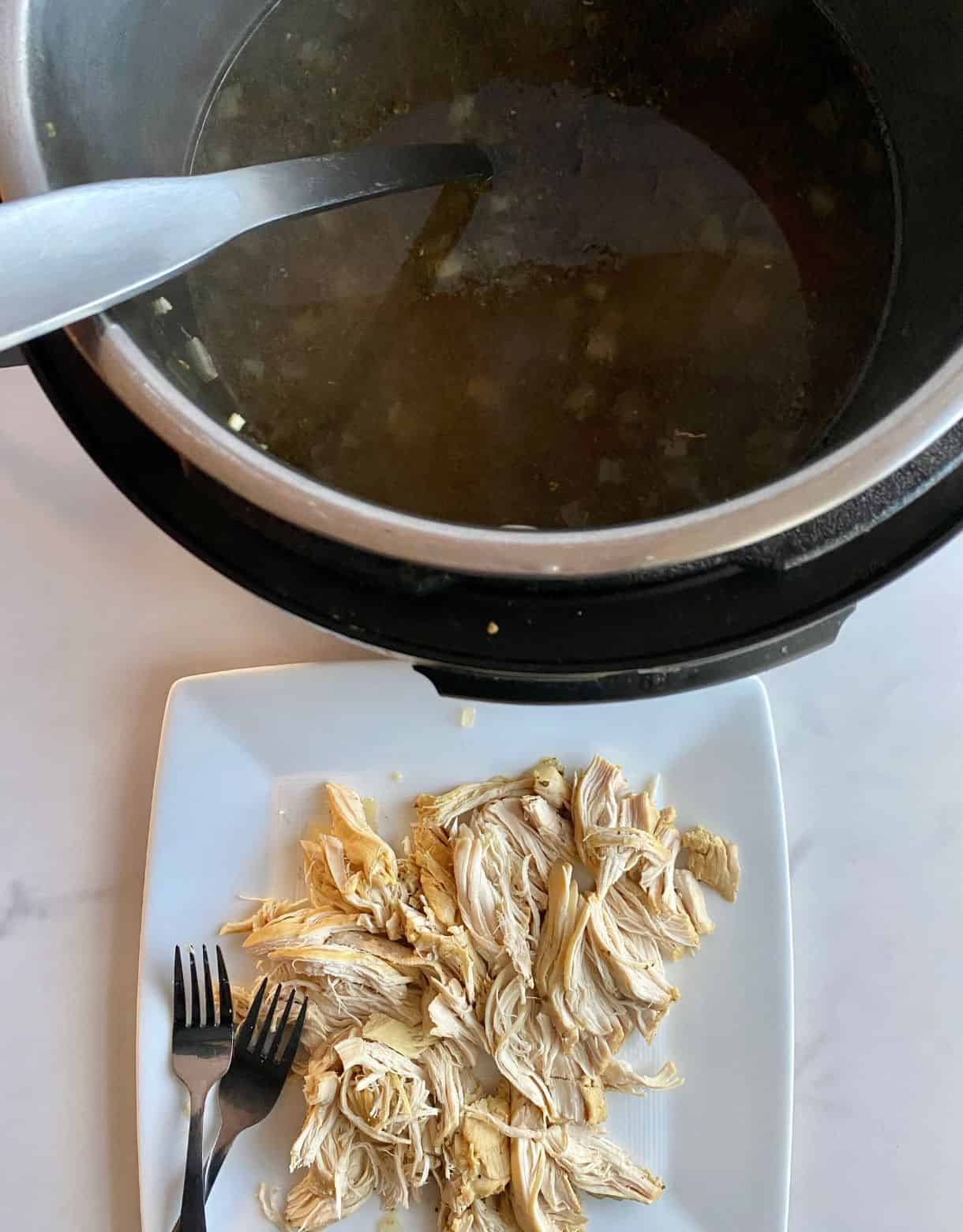 A slow cooker of soup and a plate with the chicken for the soup shredded with 2 forks.