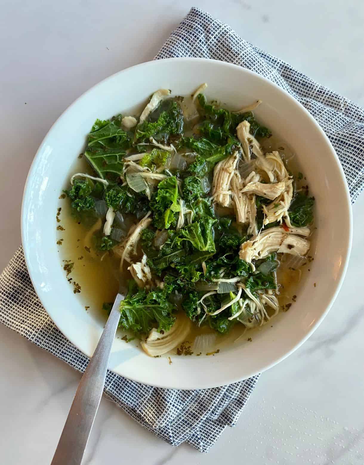 A bowl of Chicken Kale Soup with a spoon.