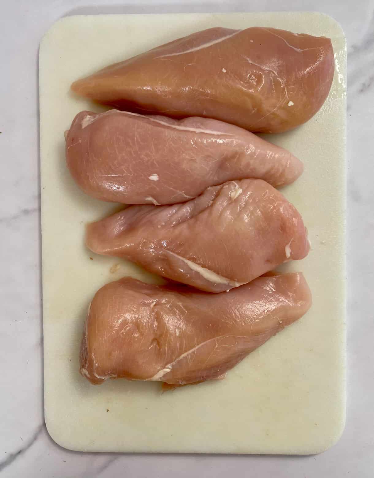 A cutting board with raw chicken.