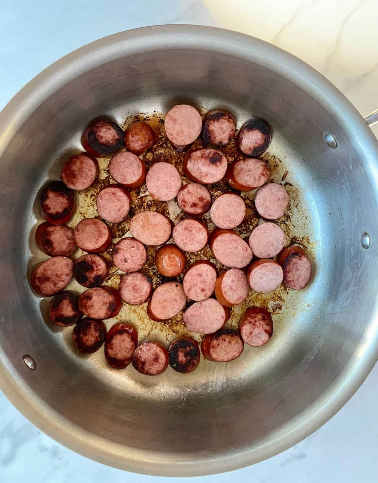 A skilled with browned sliced smoked sausage.