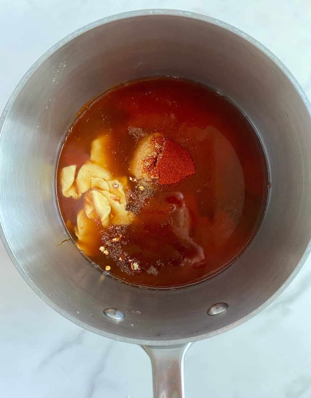 A pot with tomato sauce, vinegar, dijon mustard, brown sugar, liquid smoke, molasses and spices added but not stirred.