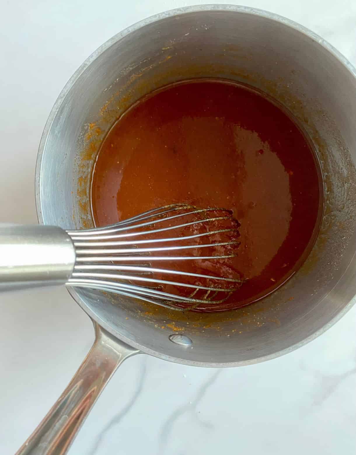 A pot with BBQ sauce ingredients stirred together and a whisk.