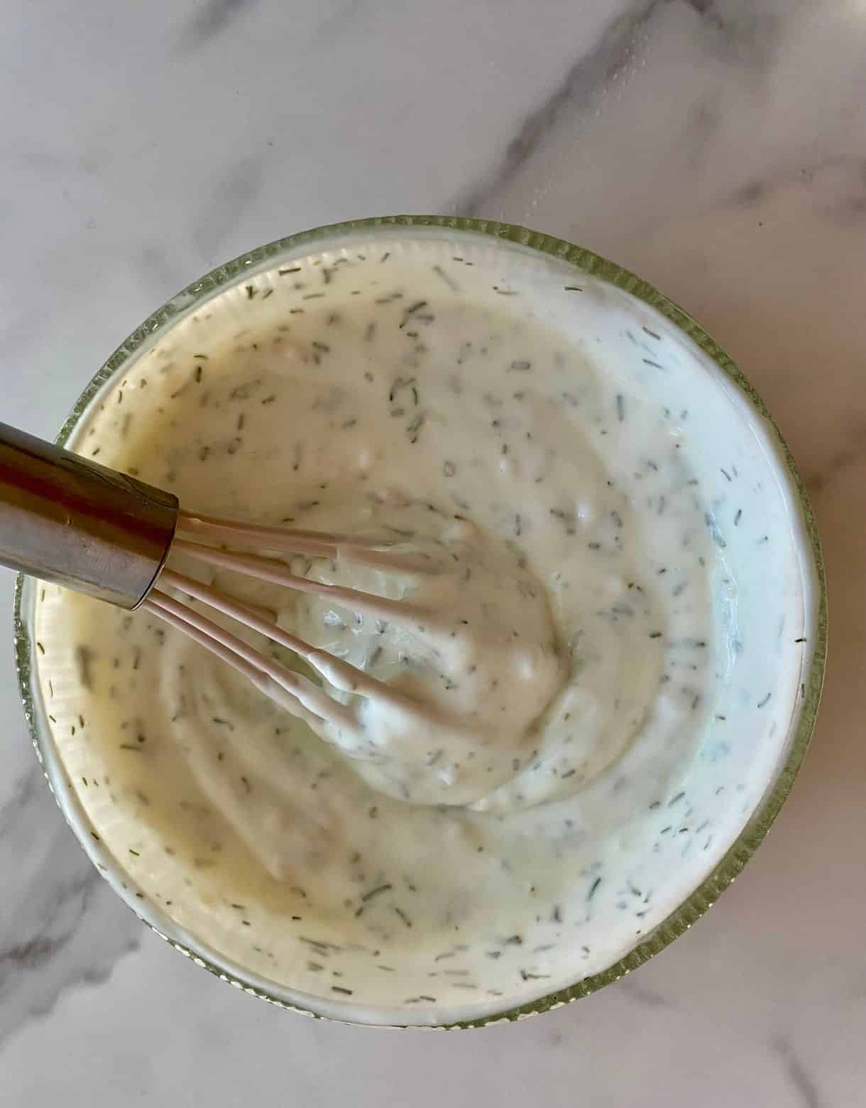 A bowl with a whisk and mixed Yogurt Dill Sauce.