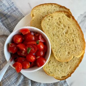 A bowl of Bruschetta Dip with a spoon and 3 slices of toasted buttered bread.