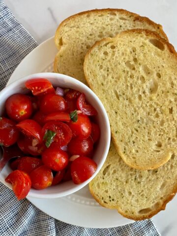 A bowl of Bruschetta Dip with a spoon and 3 slices of toasted buttered bread.