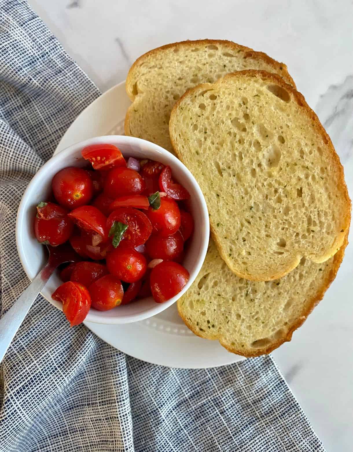 A bowl of Bruschetta Dip with a spoon and 3 slices of toasted buttered bread.