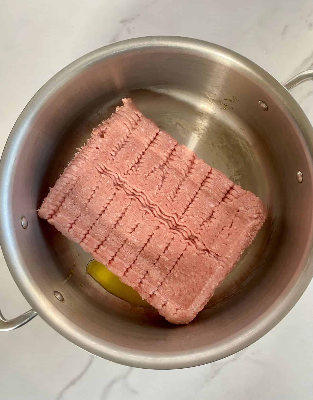 A pot with olive oil added and raw ground turkey.