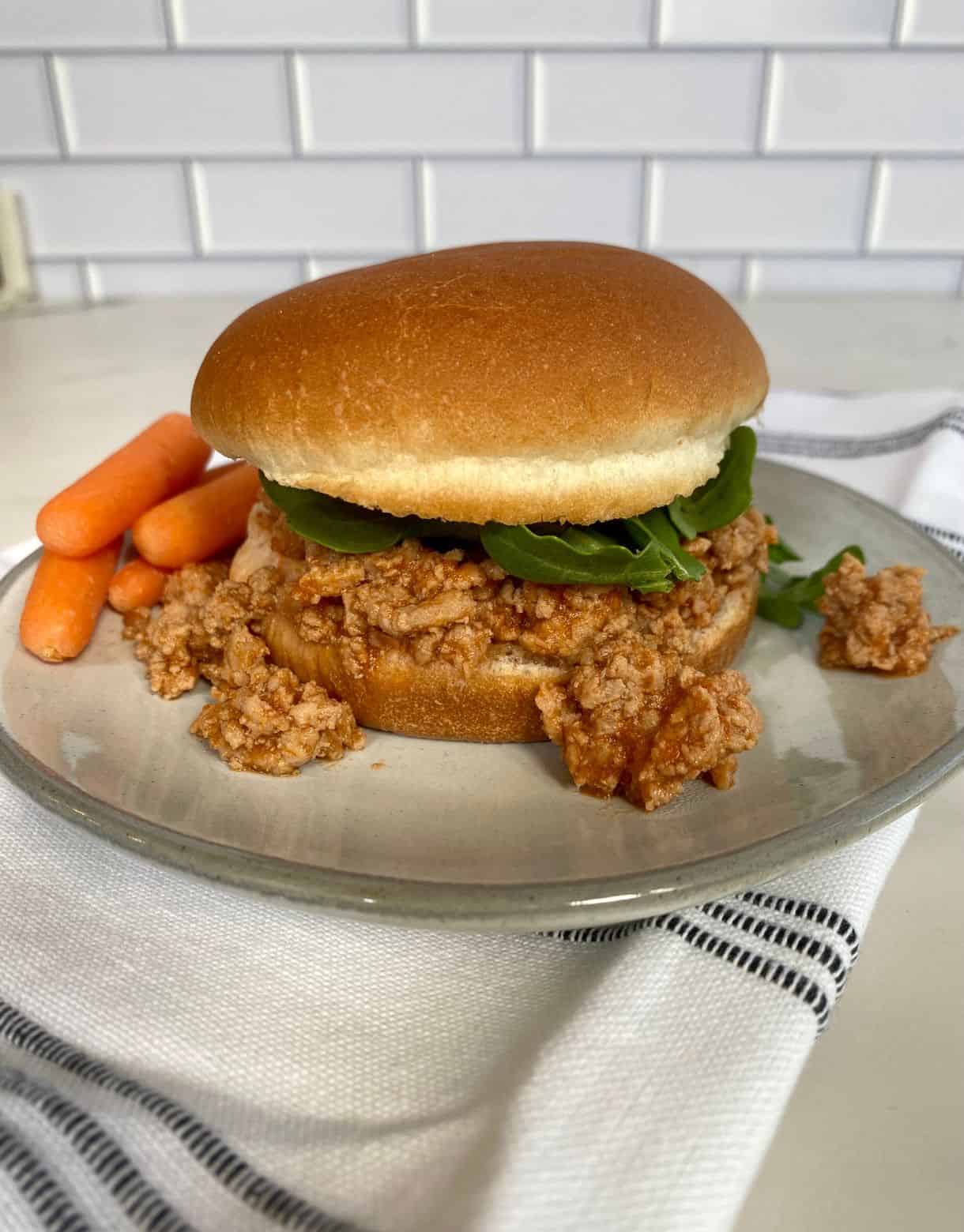 A Buffalo Sloppy Joe sandwich on a plate with baby carrots.