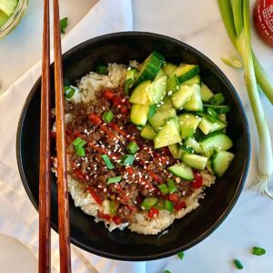 A Bulgogi Bowl with seasoned beef served over cauliflower rice and topped with sliced green onions, sesame seeds, pickled cucumbers and sriracha sauce.