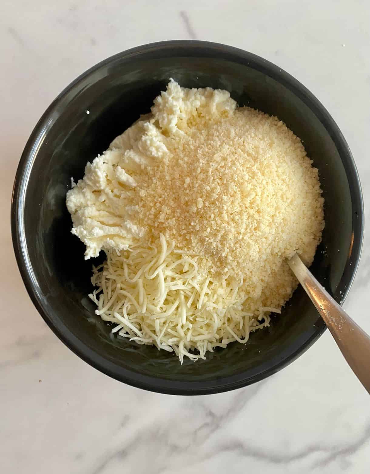 A bowl of ricotta, parmesan and mozzarella cheese with a spoon.