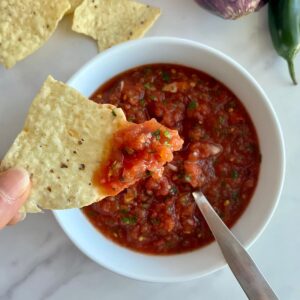 A bowl of Jalapeno Salsa with a spoon and a chip dipped in the salsa.