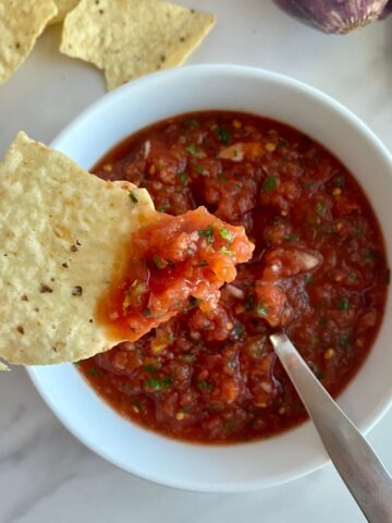 A bowl of Jalapeno Salsa with a spoon and a chip dipped in the salsa.
