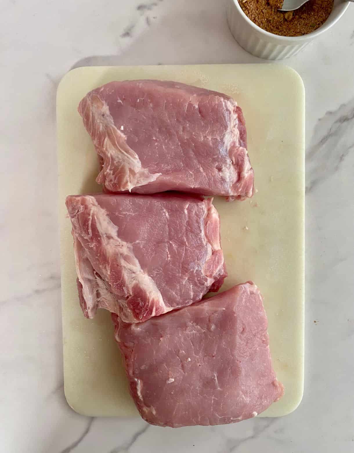 A pork loin cut into 3 pieces on a cutting board and a dish with a spice rub mix.