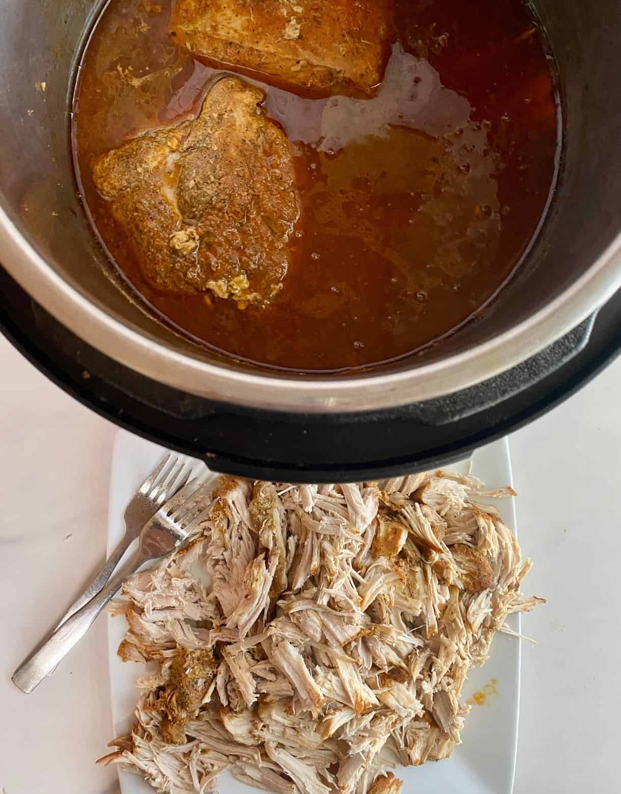 A plate with shredded cooked pork loin and a slow cooker with the cooking juices.
