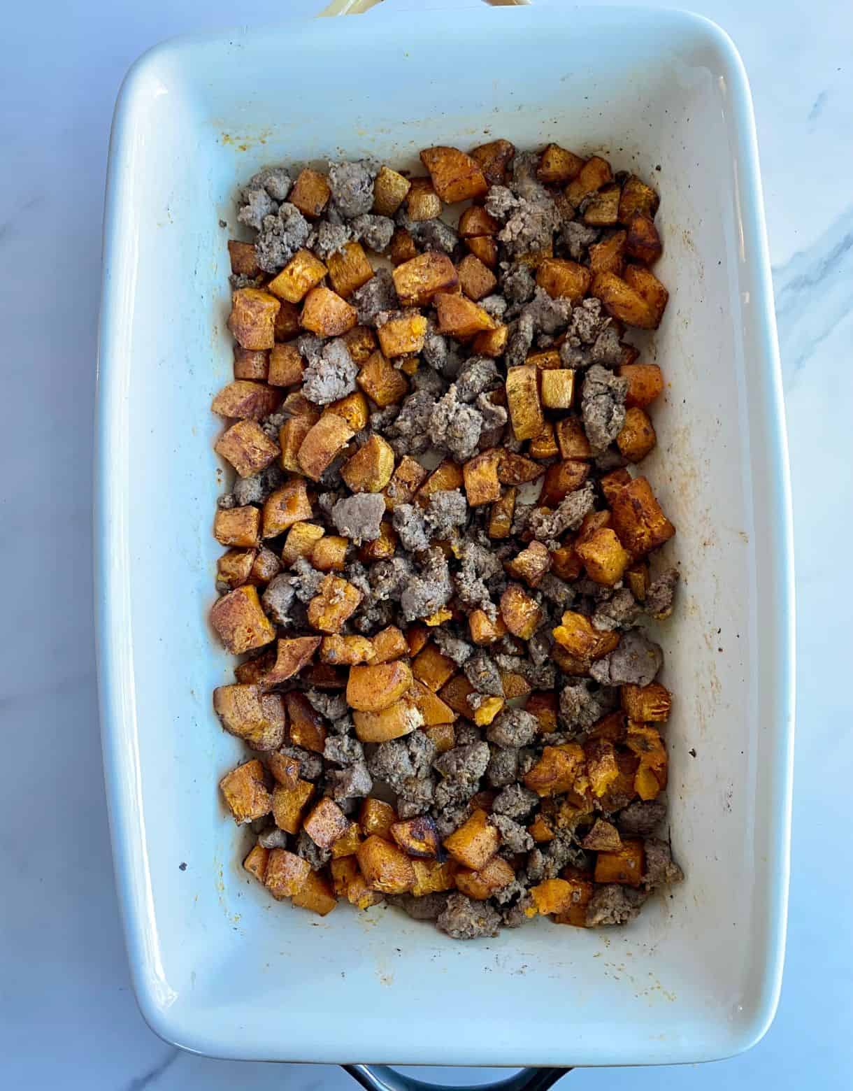 A baking dish with cooked sweet potatoes and turkey sausage.