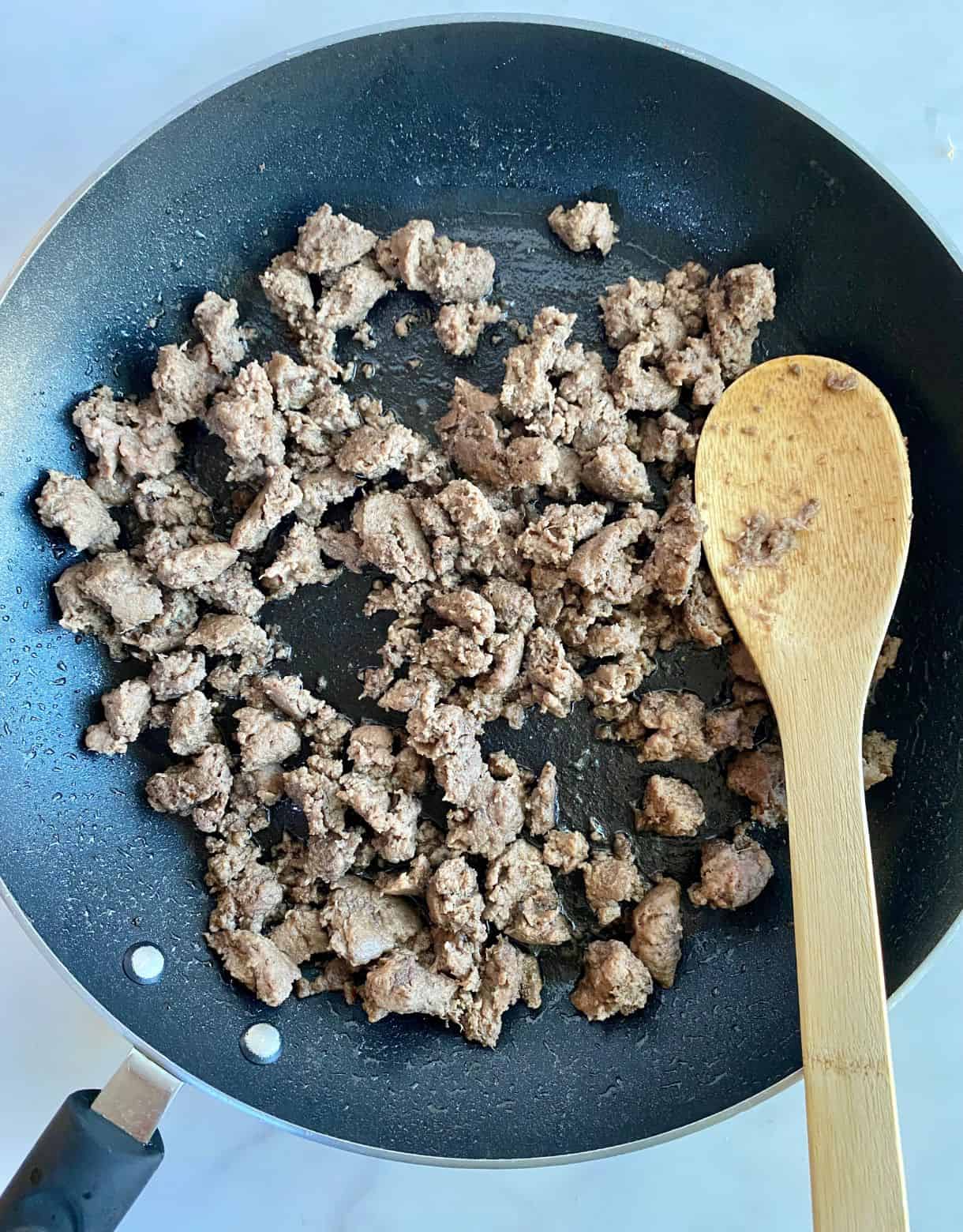 A pan with cooked and crumbled turkey sausage and a wooden spoon.
