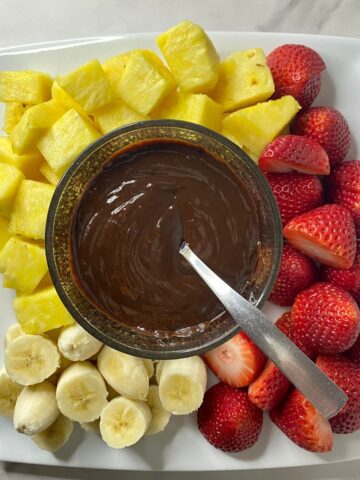 A plate with melted Chocolate Fondue surrounded by sliced pineapple, strawberries and bananas.