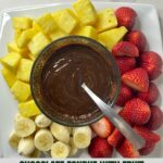 A plate with melted Chocolate Fondue surrounded by sliced pineapple, strawberries and bananas.