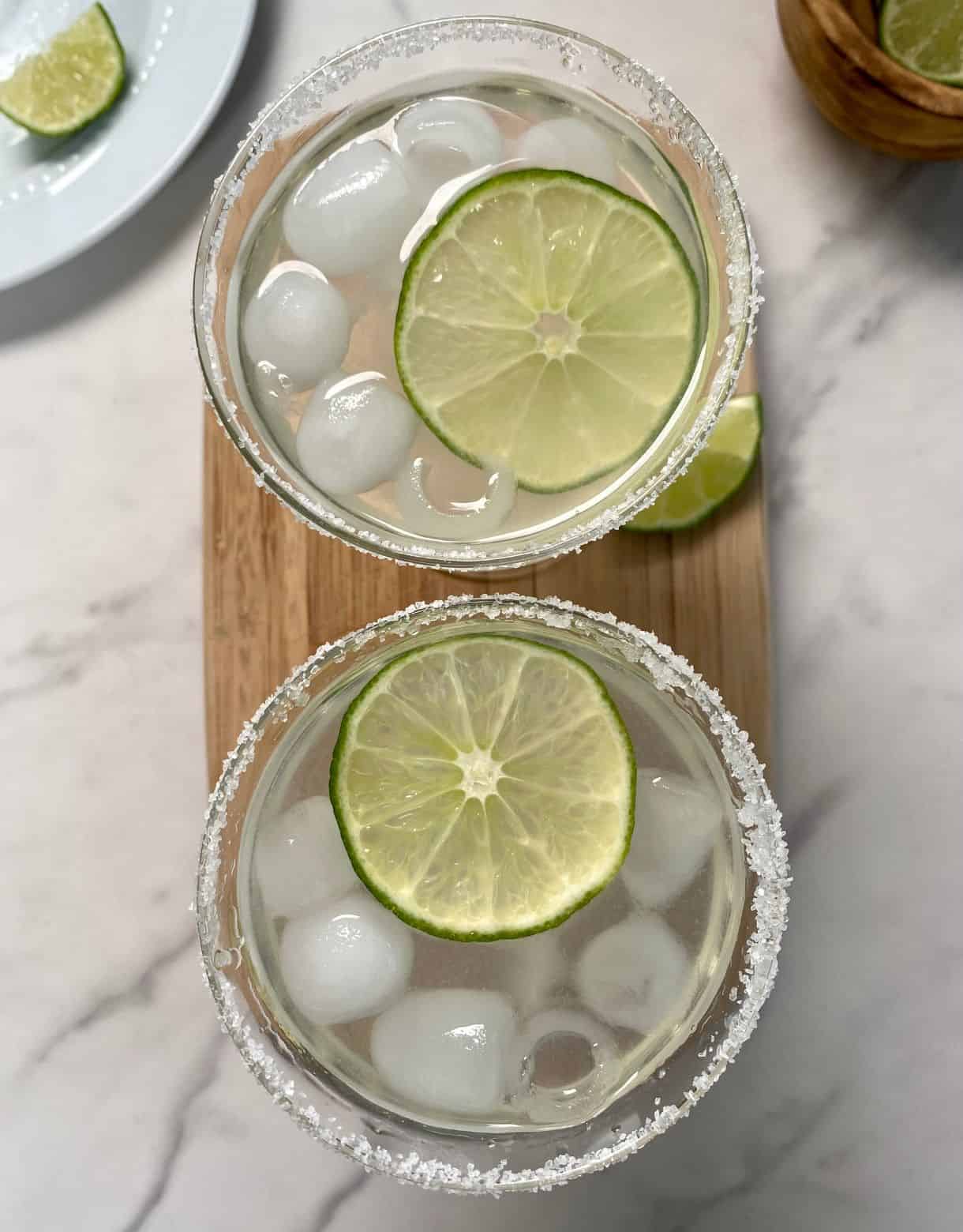 Two Cointreau Margaritas shot from over top with ice, salted rims and lime wheels in them.