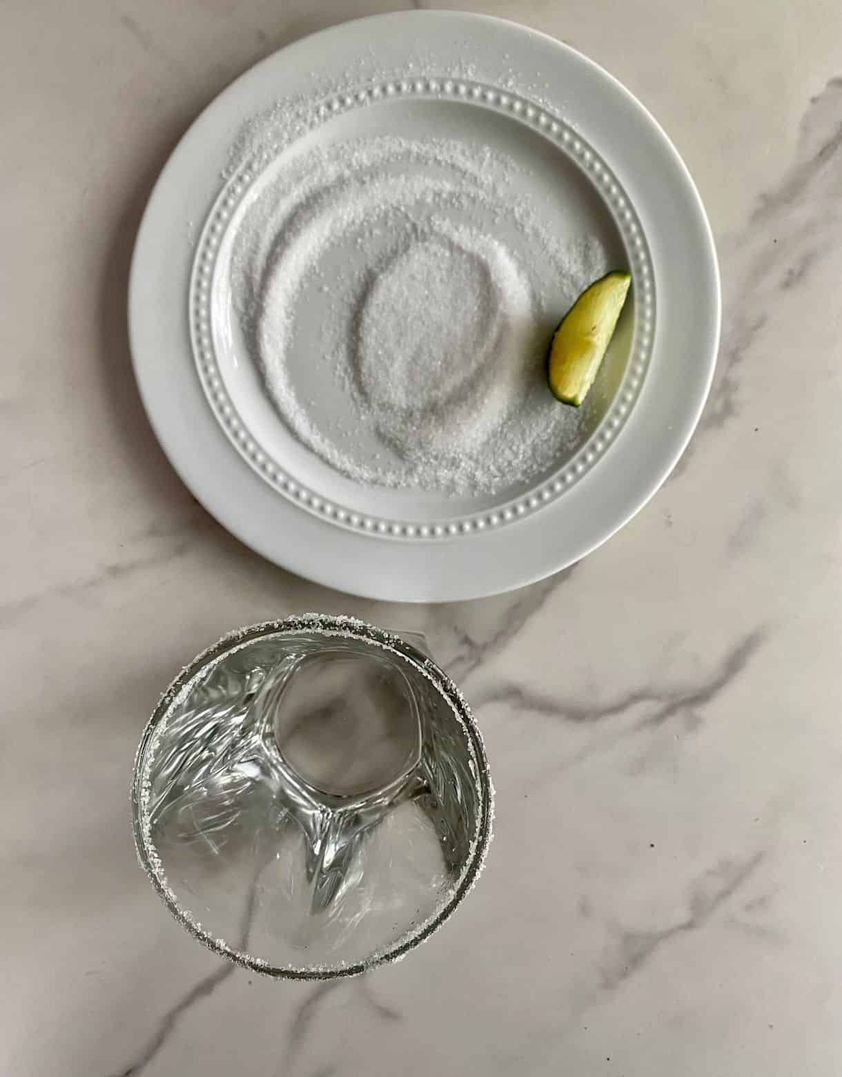 A glass with a salted rim and a plate with salt and a lime.