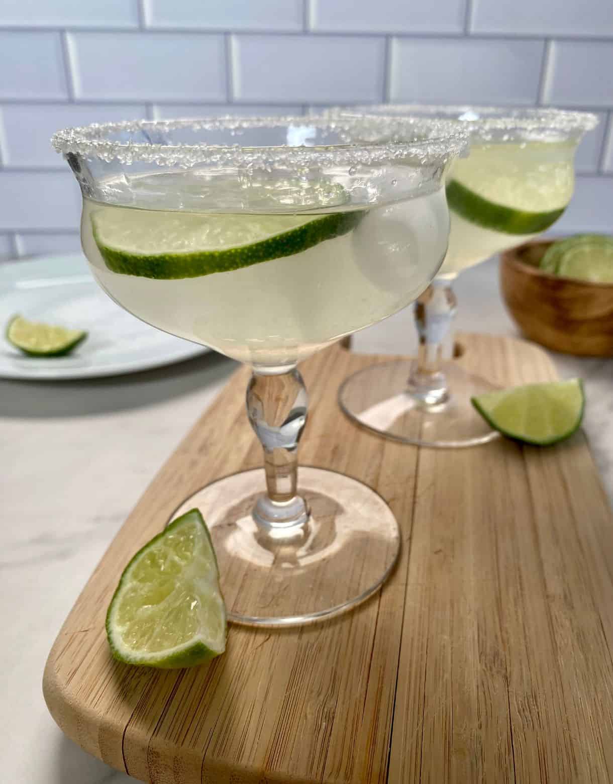 Two glasses of Cointreau Margaritas with wedges of lime and salted rims.