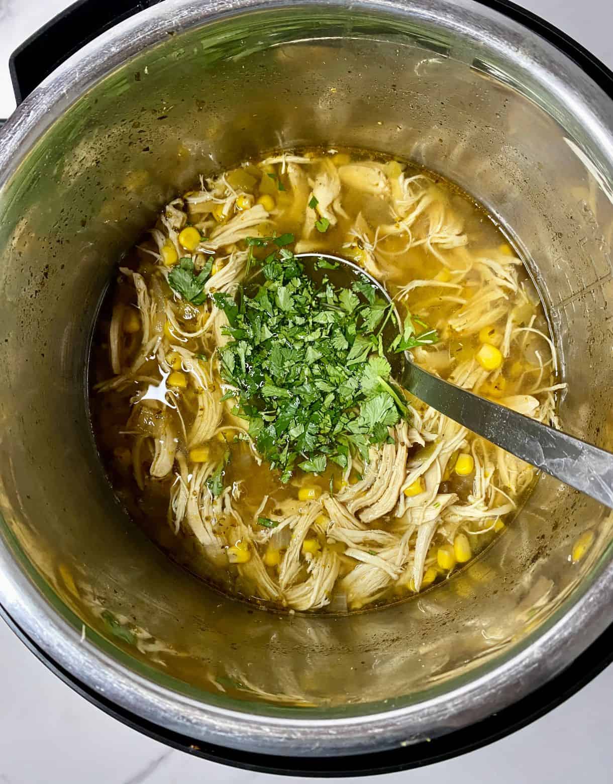 A slow cooker of Green Chile Chicken Soup with cilantro added but not yet stirred.