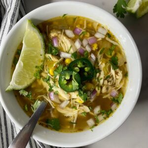A bowl of Green Chile Chicken Soup with a spoon and a wedge of lime.