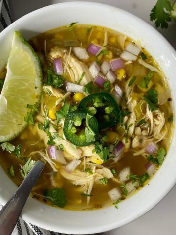 A bowl of Green Chile Chicken Soup with a spoon and a wedge of lime.