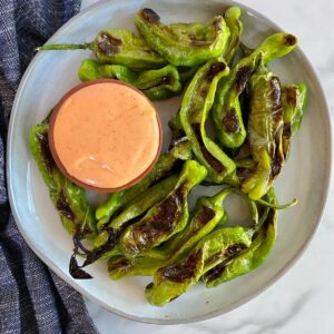 A plate of Grilled Shishito Peppers with Sriracha Mayo dipping sauce.