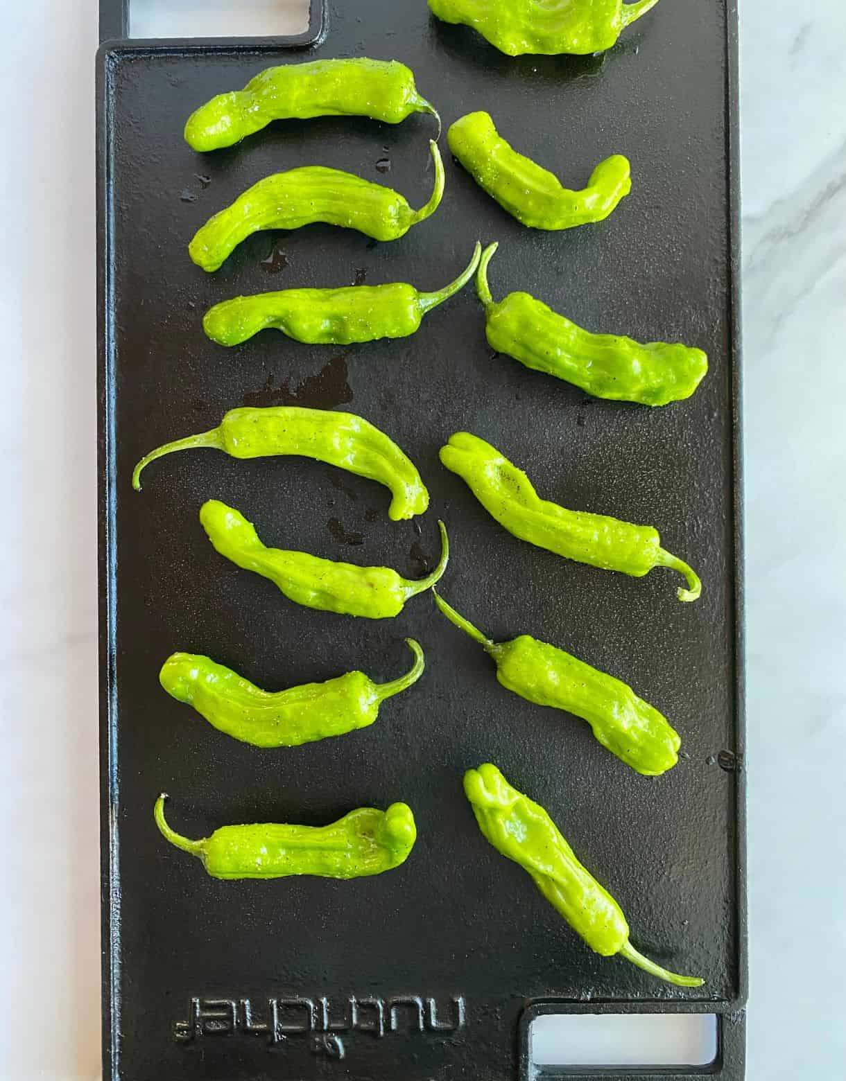 A grill pan with shishito peppers cooking on it.