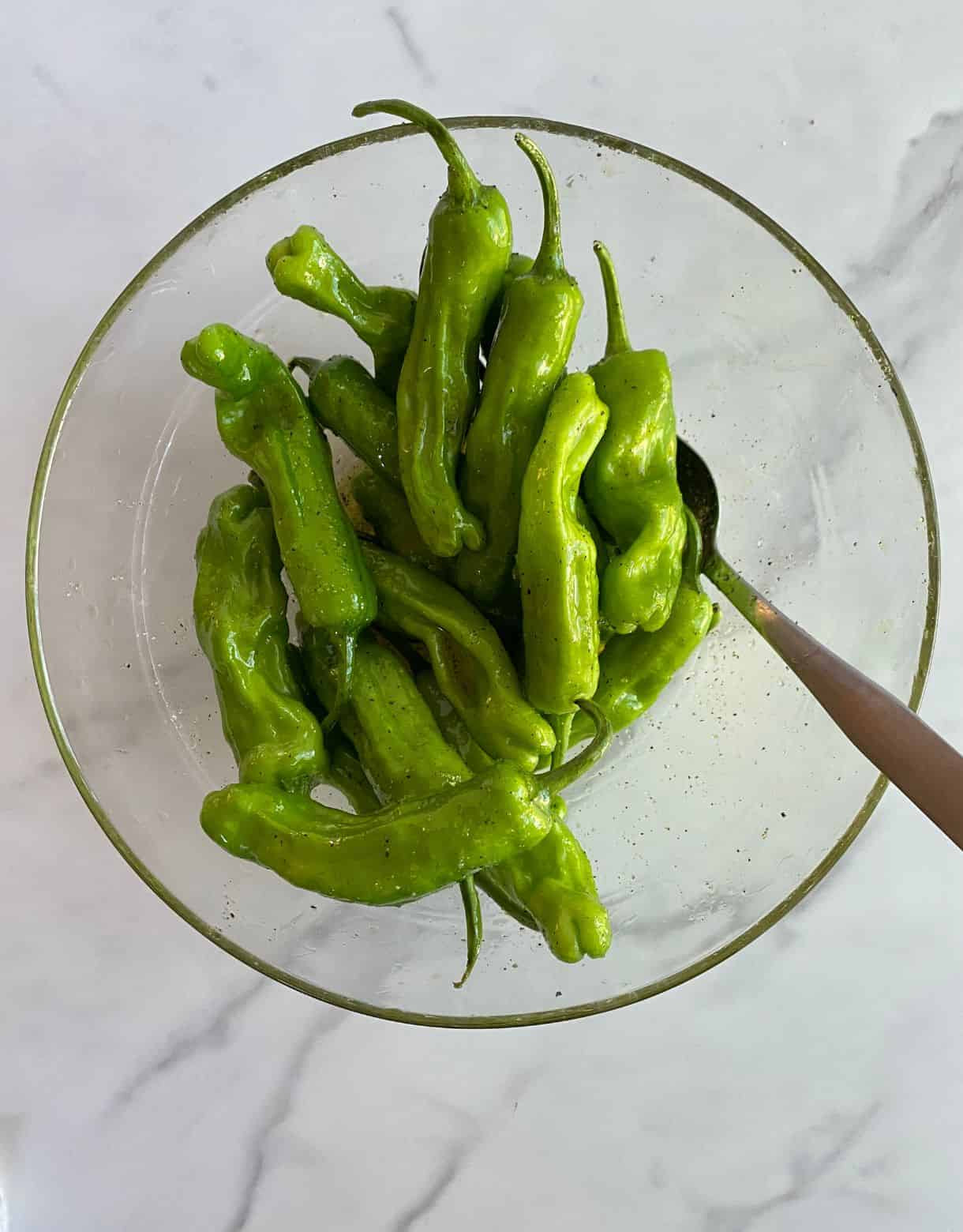 A bowl of seasoned shishito peppers ready to grill.