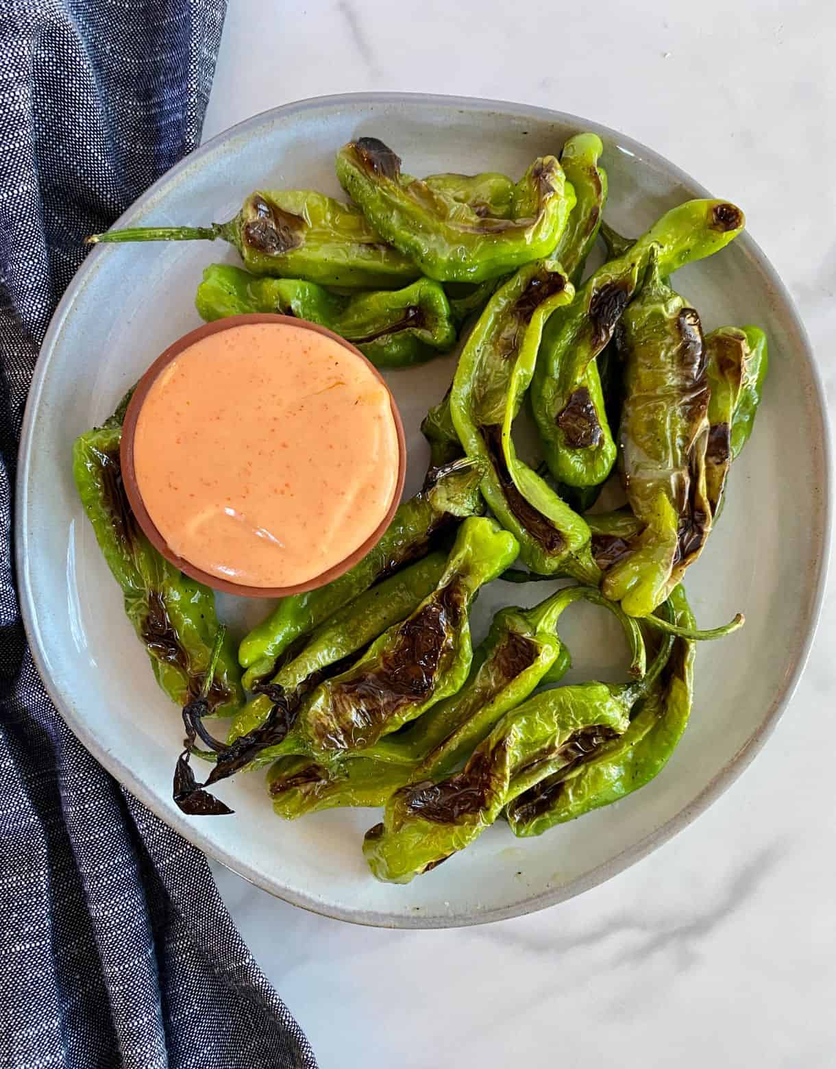A plate of Grilled Shishito Peppers with Sriracha Mayo dipping sauce.