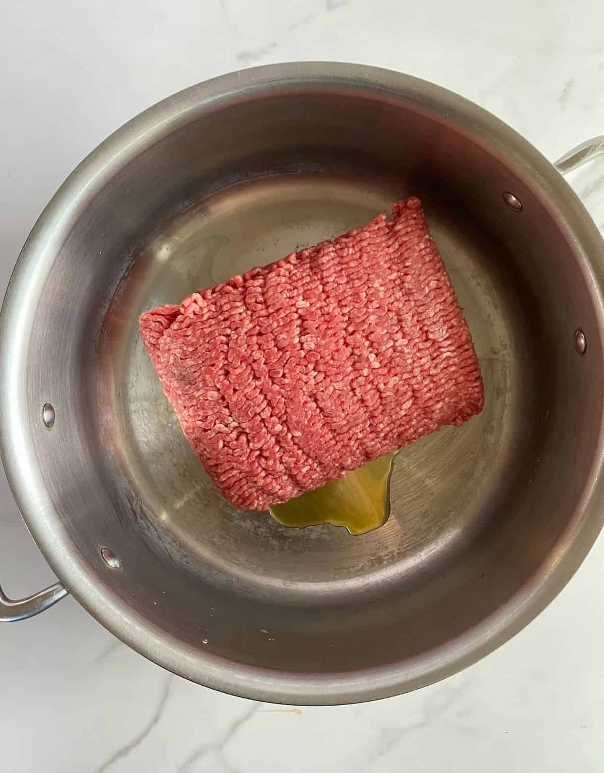 A pot with olive oil and ground beef added.