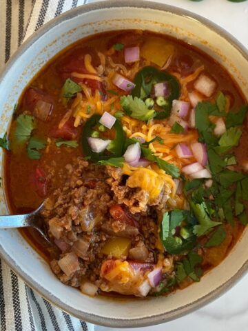 A bowl of Sweet and Spicy Chili topped with cheese, sliced jalapenos diced onion and cilantro.