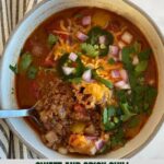 A bowl of Sweet and Spicy Chili topped with cheese, sliced jalapenos diced onion and cilantro.