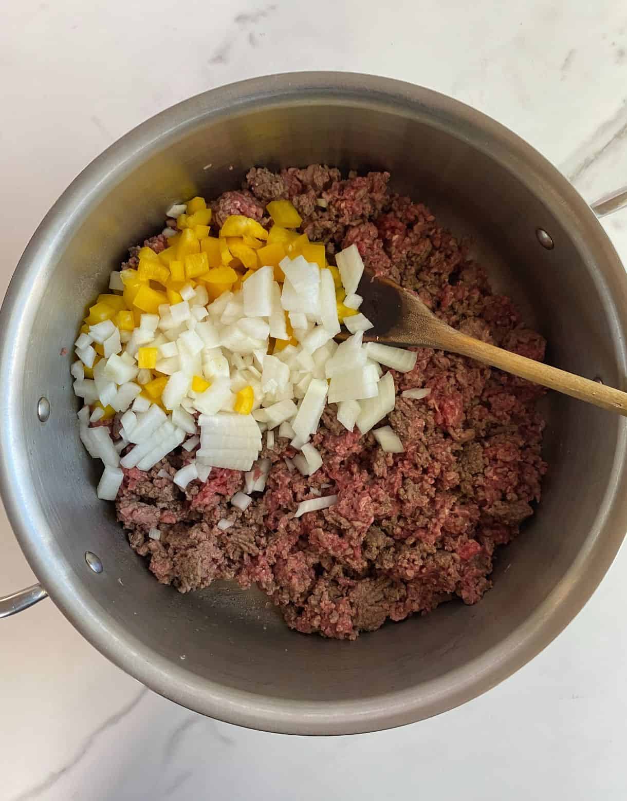 A pot with mostly browned beef with raw bell pepper and onion added.
