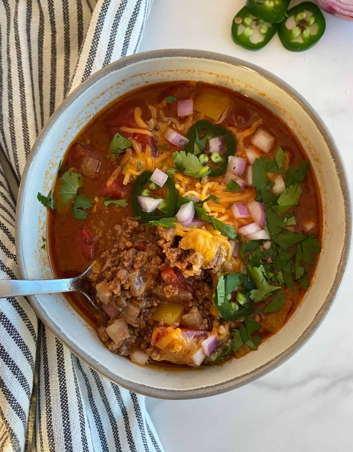 A bowl of Sweet and Spicy Chili topped with cheese, sliced jalapenos diced onion and cilantro.