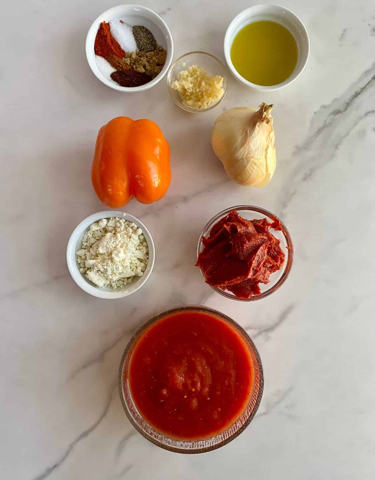 Ingredients for Turkish Shakshuka. Crushed tomatoes, tomato paste, feta cheese, onion, bell pepper, garlic, olive oil, salt, pepper, smoked paprika, chili powder, sugar and cayenne pepper.