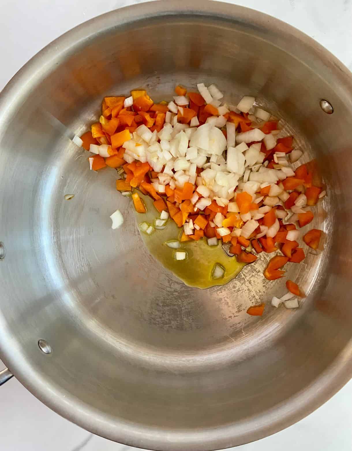 A pot with olive oil and raw onions and bell peppers ready to saute.