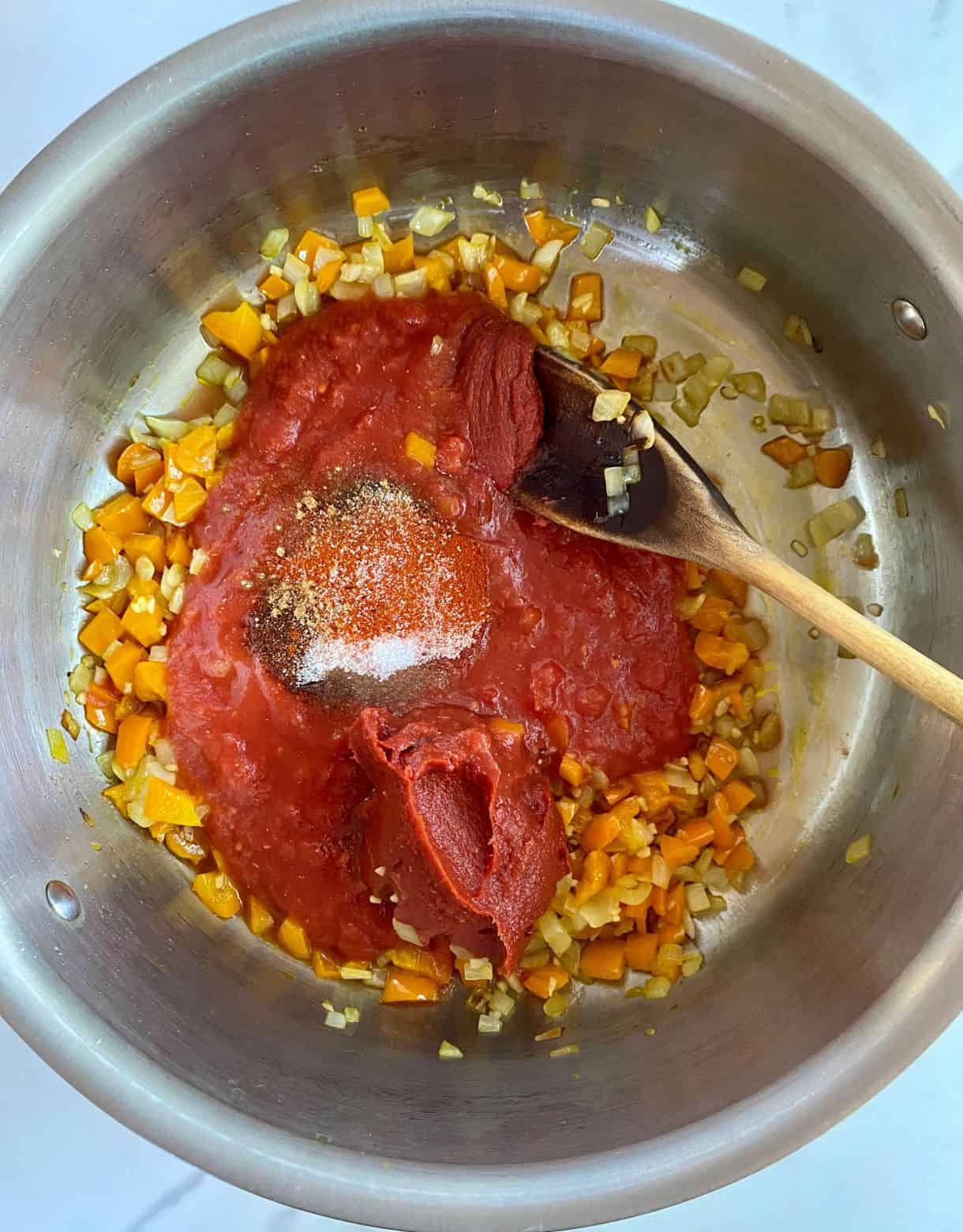 A pot with sauteed onions and bell peppers with crushed tomatoes and spices added but not stirred.